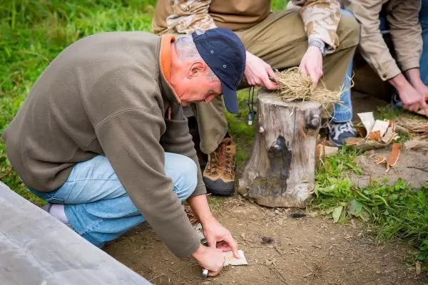 Person bereitet Zunder auf dem Boden vor beim Survival Training