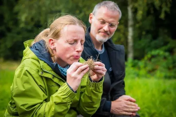 Person bläst in ein Bündel aus Gras, während eine andere Person zuschaut beim Survival Training