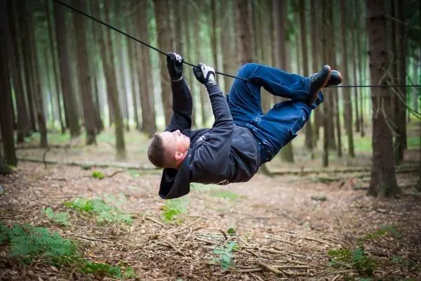 Person hängt an einem Seil zwischen Bäumen im Wald