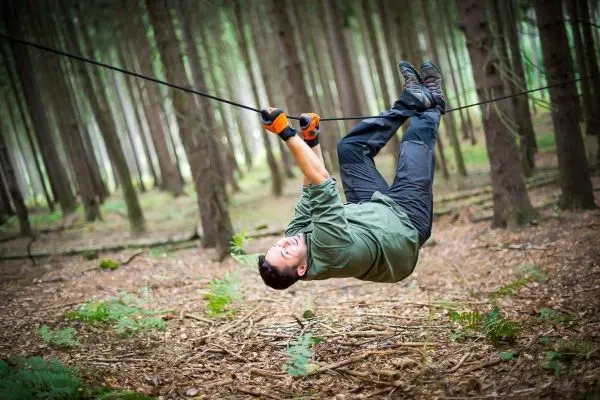 Person hängt kopfüber an einem Seil zwischen Bäumen beim Überlebenstraining