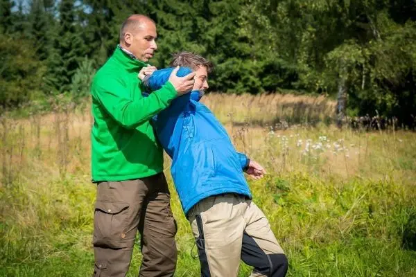 Person hilft anderer Person beim Anziehen einer Jacke im Freien