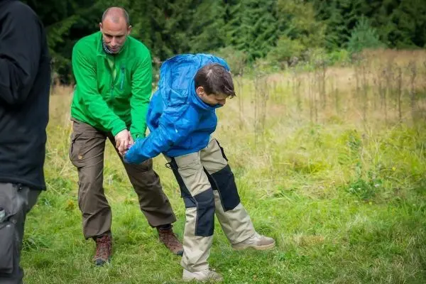 Person hilft anderer Person beim Gehen auf Grasfläche