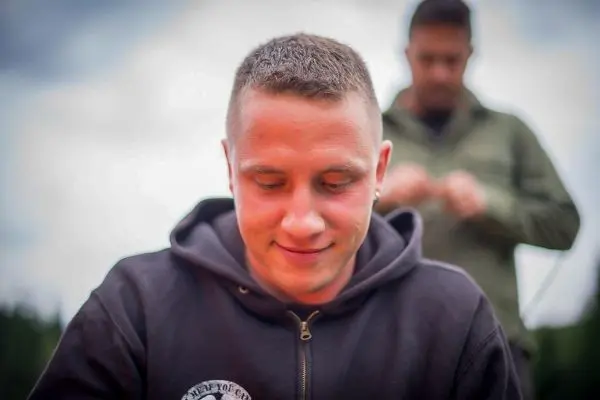 Person mit kurzem Haar und Kapuzenpullover schaut nach unten, im Hintergrund eine weitere Person