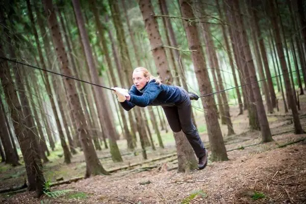 Person schwingt an einer selbstgebauten Seilbrücke durch den Wald