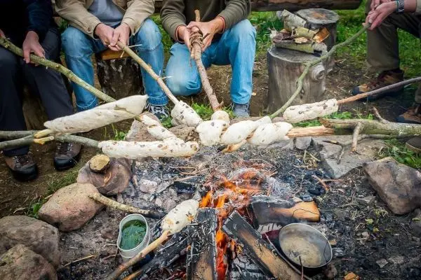 Personen halten Stockbrot über ein Feuer beim Überlebenstraining