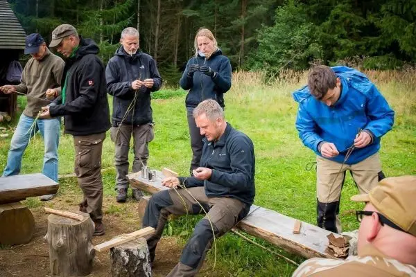 Teilnehmer flechten mit Pflanzenmaterial auf einer Holzbank im Freien