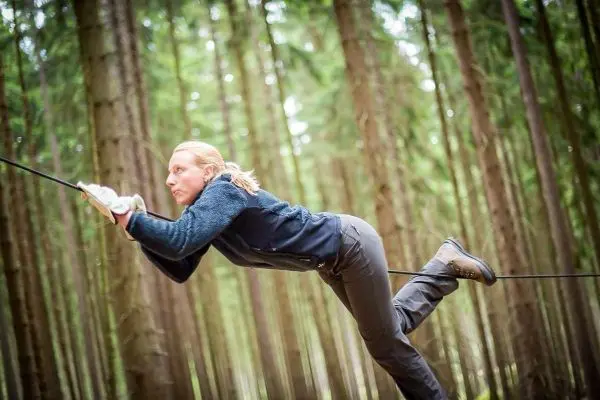 Überquert eine selbstgebaute Seilbrücke zwischen Bäumen im Wald