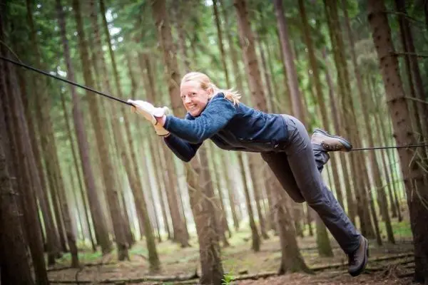 Überquert eine selbstgebaute Seilbrücke zwischen Bäumen im Wald