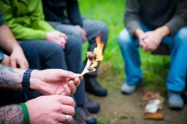 Zunder brennt in der Hand, während Personen im Hintergrund sitzen