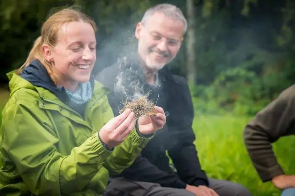 Zunder glimmt in der Hand einer Person, Rauch steigt auf