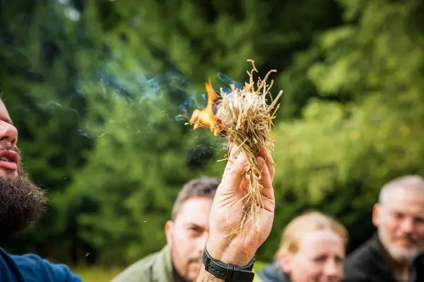 Zunder glimmt und raucht in der Hand, während Zuschauer aufmerksam beobachten