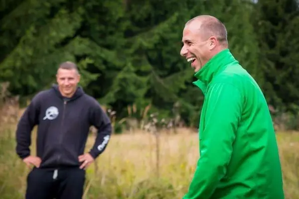 Zwei Männer lachen in einer Wiese, umgeben von Bäumen