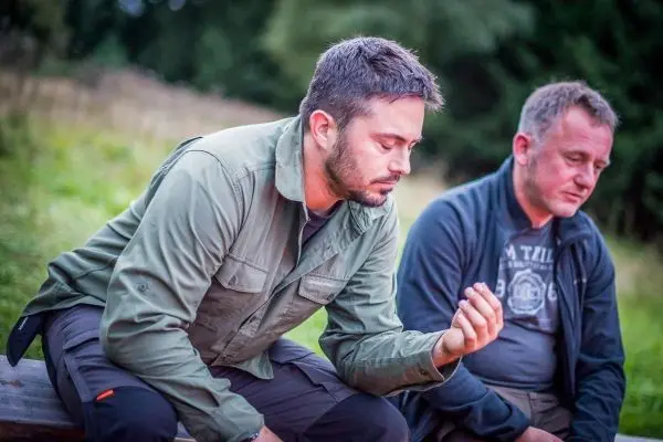 Zwei Männer sitzen auf einer Bank und betrachten aufmerksam einen kleinen Gegenstand in der Hand