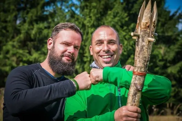 Zwei Männer zeigen Daumen hoch und halten einen selbstgebauten Stock mit Spitzen