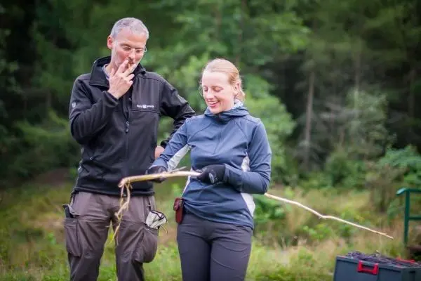 Zwei Personen betrachten gemeinsam einen langen Stock im Wald