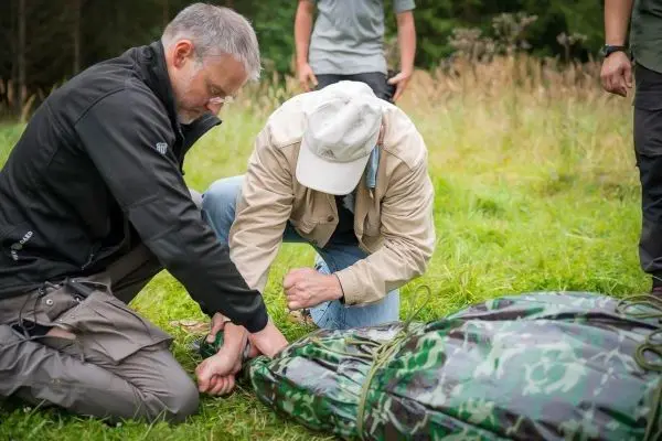 Zwei Personen binden eine improvisierte Trage aus einem camouflagefarbenen Material