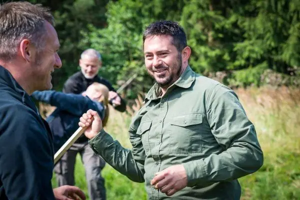 Zwei Personen halten einen Stock und lächeln sich an, im Hintergrund weitere Teilnehmer