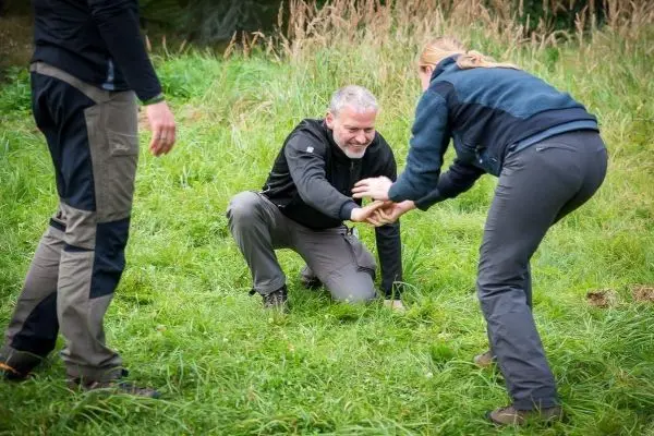 Zwei Personen helfen einem Mann, der auf dem Boden sitzt, beim Aufstehen
