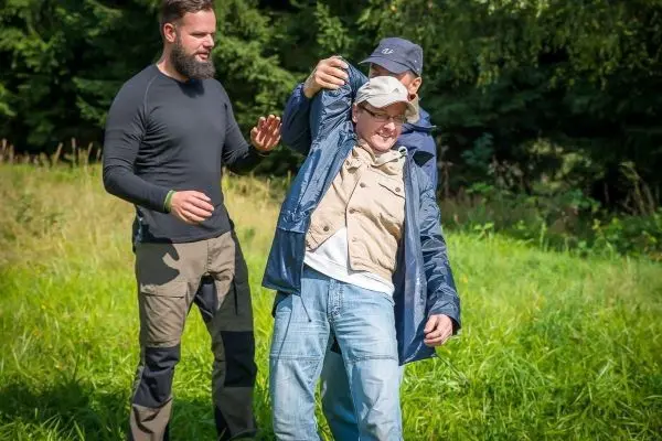 Zwei Personen helfen einem Mann, der in einer Jacke steht, aufrecht zu bleiben