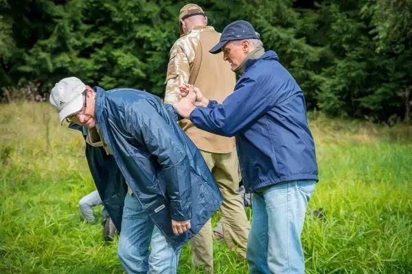 Zwei Personen helfen sich gegenseitig beim Anlegen einer improvisierten Trage