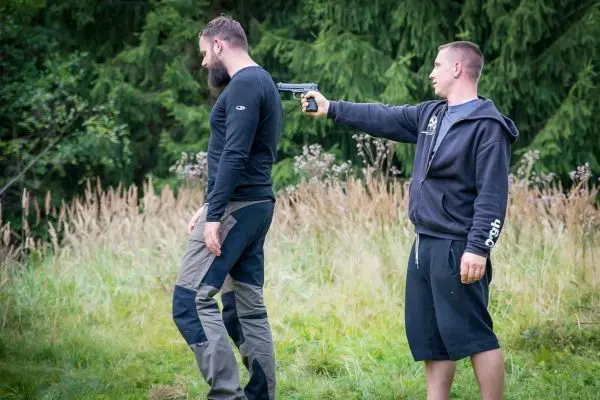 Zwei Personen in einem Feld, eine hält eine Pistole auf die andere