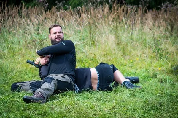 Zwei Personen liegen im Gras, eine Person hält die andere in einer kontrollierenden Position