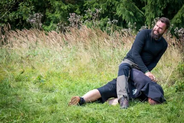 Zwei Personen liegen im Gras, eine Person sitzt auf der anderen und hält sie fest