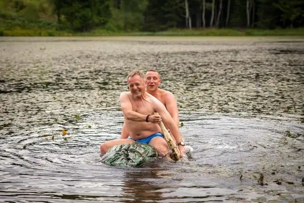 Zwei Personen sitzen auf einem großen, schwimmenden Objekt im Wasser und paddeln mit einem Stock