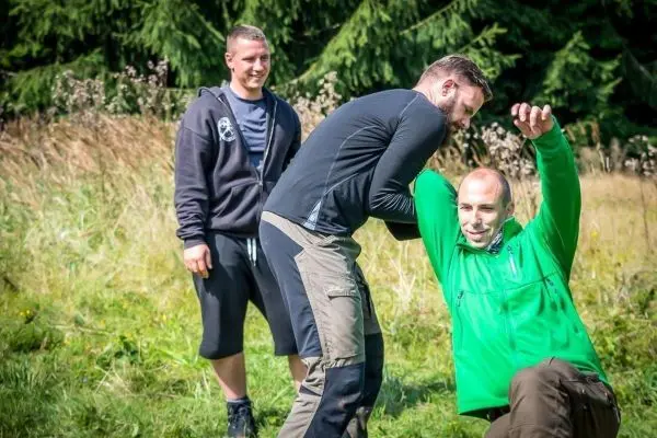 Zwei Personen üben eine Selbstverteidigungstechnik im Freien, während eine dritte Person zuschaut