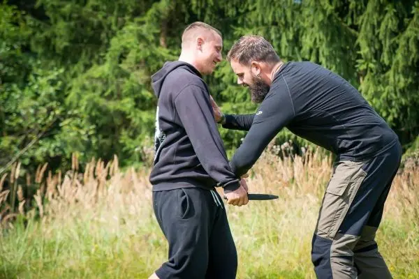 Zwei Personen üben eine Selbstverteidigungstechnik mit einem Messer im Freien