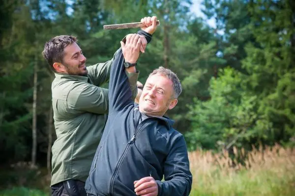 Zwei Personen üben eine Selbstverteidigungstechnik mit einem Stock im Freien