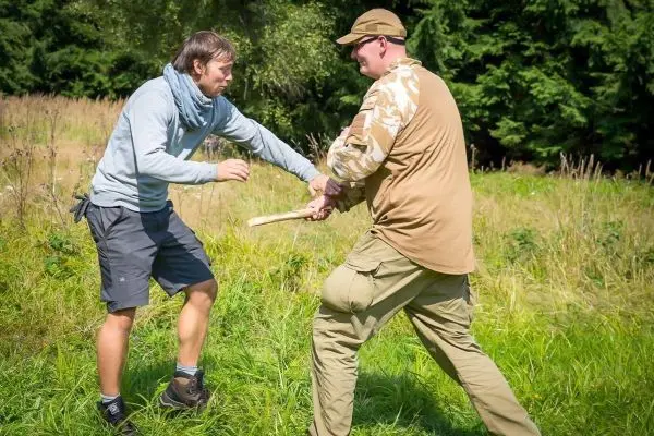 Zwei Personen üben eine Technik mit einem Holzstock in einer Wiese