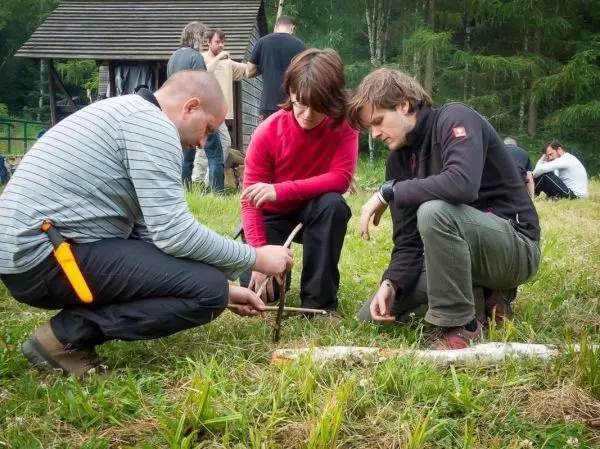 Drei Personen arbeiten gemeinsam an einer Holzarbeit im Gras