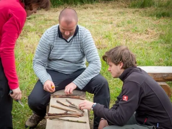 Drei Personen bearbeiten Holzstücke auf einer Bank im Freien