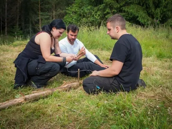 Drei Personen sitzen im Gras und arbeiten an einem Holzstück
