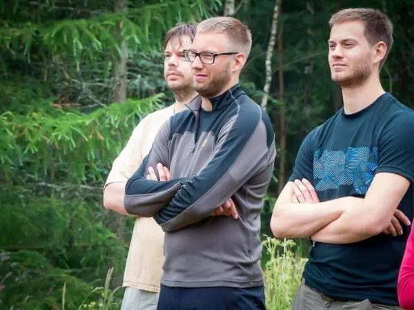 Drei Personen stehen im Wald mit verschränkten Armen