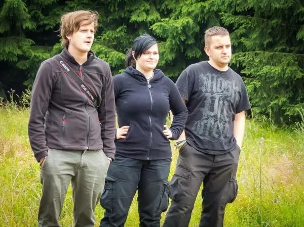 Drei Personen stehen in einer Wiese vor einem Wald