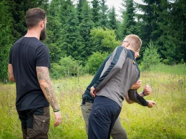 Drei Personen üben eine Selbstverteidigungstechnik im Freien