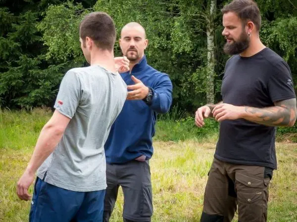 Drei Personen üben eine Technik im Freien auf einer Wiese
