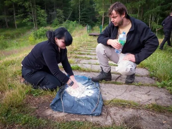 Frau knetet eine Mischung auf einem blauen Tuch, Mann beobachtet mit Wasserflasche