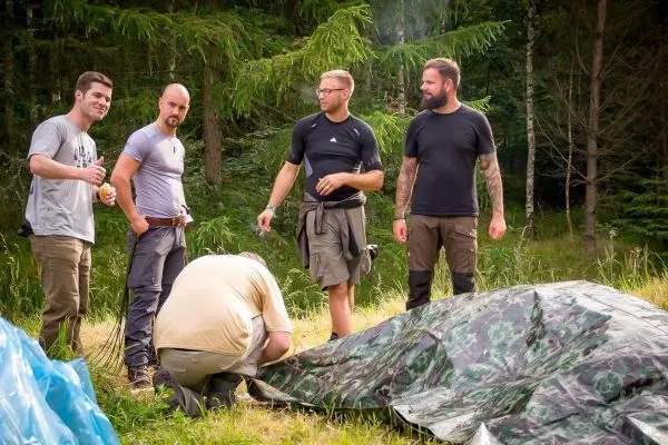 Fünf Personen stehen um ein Tarp und bereiten eine Notunterkunft vor