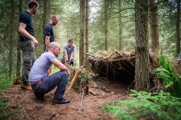 Gruppe betrachtet selbstgebaute Tarp-Notunterkunft im Wald