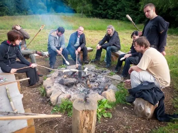 Gruppe sitzt um ein Lagerfeuer und röstet Lebensmittel auf Stockspießen