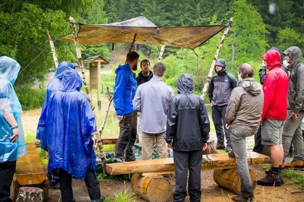 Gruppe steht unter einer Tarp-Notunterkunft und hört einem Vortrag zu
