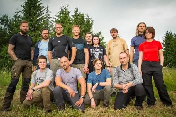 Gruppierung von zwölf Personen im Freien, umgeben von Bäumen und Gras