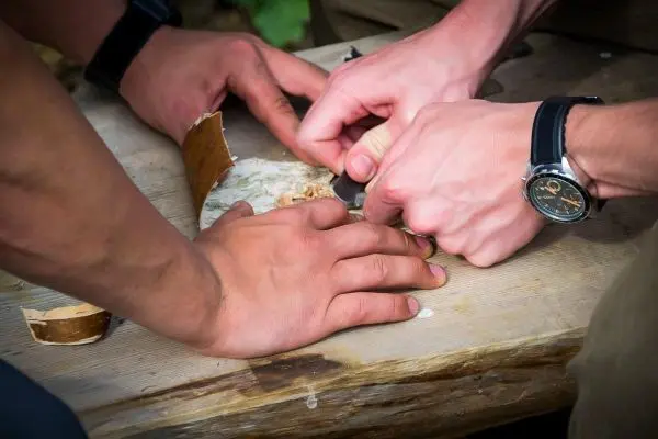 Hände bearbeiten einen Holzstück auf einem Tisch beim Überlebenstraining