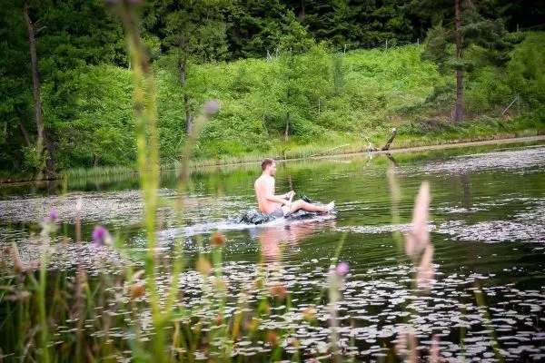 Junge paddelt auf einem improvisierten Floß über einen ruhigen See