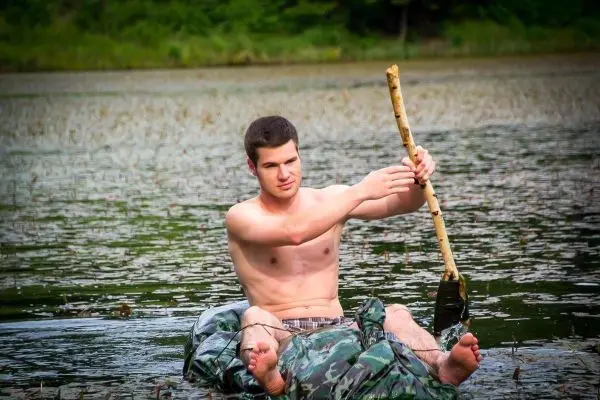 Junge paddelt mit improvisiertem Paddel in einem Gewässer