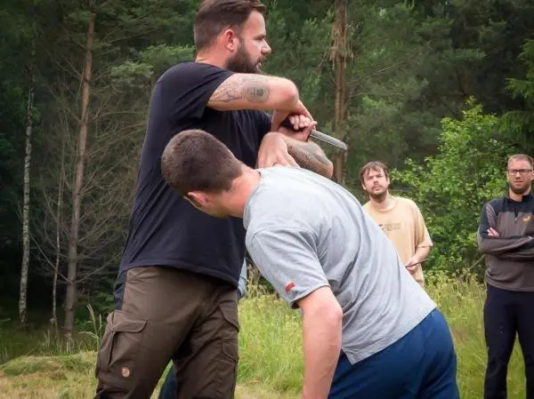 Kampftechniken werden demonstriert, während ein Teilnehmer einen anderen mit einem Messer kontrolliert