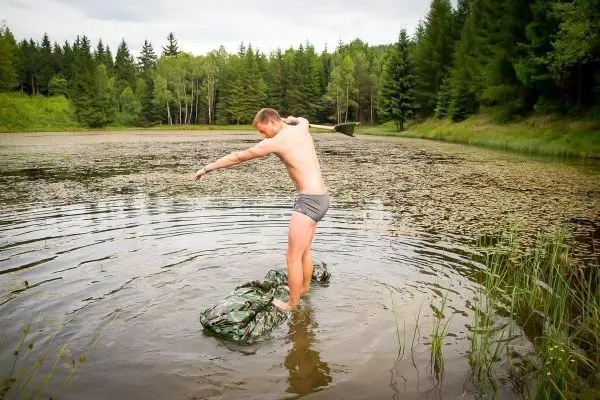 Mann balanciert auf einem camouflagefarbenen Sack im Wasser eines Teiches